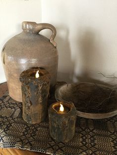 two candles are lit in front of an old jug