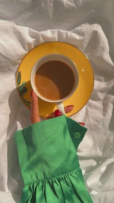 a woman's hand holding a cup of coffee on top of a yellow plate