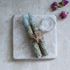 three green candles on a marble tray with flowers and ice cubes in the background