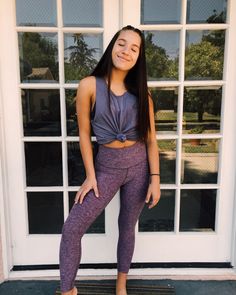 a woman standing in front of a white door wearing purple leggings and smiling