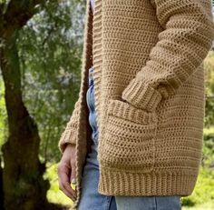 a man wearing a brown crochet sweater and jeans standing next to a tree