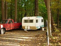 a red truck pulling a trailer in the woods with a camper attached to it