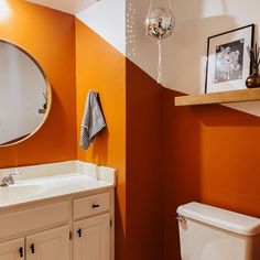 a white toilet sitting next to a sink in a bathroom under a large round mirror