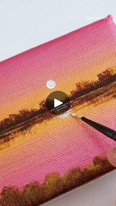 someone is painting an orange and pink sunset on a piece of canvas with a paintbrush