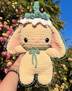 a hand holding up a crocheted stuffed animal in front of some pink flowers