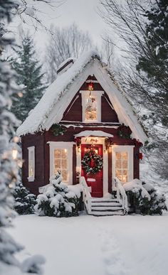 a small red house covered in snow with wreaths and lights on the front door