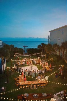 a group of people standing around a table on top of a lush green field next to the ocean