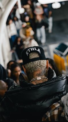 a man with tattoos on his head wearing a black hat and jacket while riding an escalator