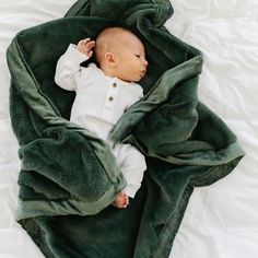 a baby wrapped in a green blanket on top of a white bedding sheet and sleeping