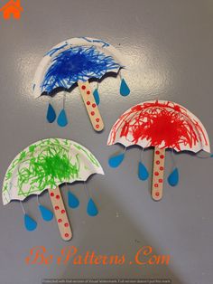 three paper umbrellas painted in different colors on a gray surface with drops of paint