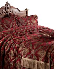 a bed with a red and gold comforter on it's headboard next to a night stand