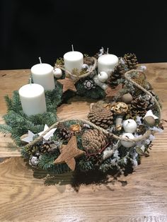 a wreath made out of pine cones, candles and other decorations on a wooden table