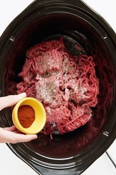 someone is holding a yellow cup in their hand while they are cooking ground meat inside the slow cooker