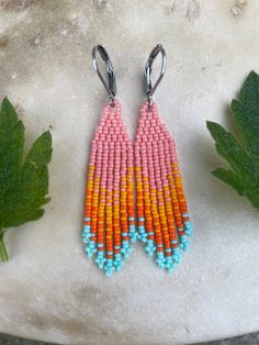 two pairs of beaded earrings sitting on top of a table next to green leaves