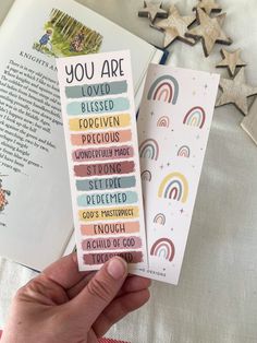 the bookmarks are being held in front of an open book with rainbows on it