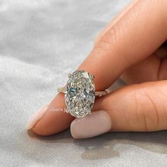 a woman's hand holding an oval diamond ring on top of her finger,