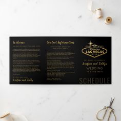 a black and gold las vegas wedding program on a marble table with scissors, tape and other items