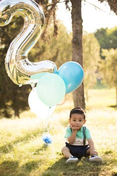 a little boy sitting in the grass with balloons and a number 2 balloon attached to it