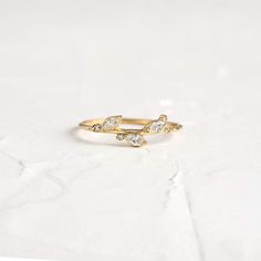 a gold ring with three small white stones on the front and back, sitting on a white surface