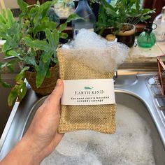 a person holding up a bag of soap in a sink filled with water and plants