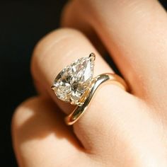 a woman's hand holding a ring with a pear shaped diamond