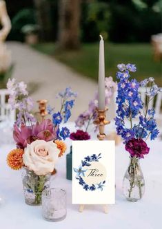 flowers in vases on top of a table with a sign and candlestick next to it