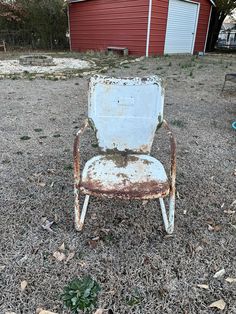 an old rusty chair sitting in the middle of a field next to a red barn