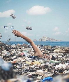 a man laying on top of a pile of trash next to the ocean with cans floating in it