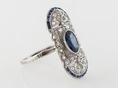 Vintage Filigree Cocktail Ring Art Deco Sapphire in Platinum $5,250.00 Vintage Filigree Cocktail Ring Art Deco Sapphire in Platinum. The center oval sapphire is approximately 1.20 carats and is a slightly darker royal blue with medium transparency. The platinum open filigree is set with rose cut diamonds. The border of this unique Art Deco oval shaped cocktail ring is set with french cut sapphires creating a frame around this lovely ring. Composition: Platinum Ring Size: 6.75 Center Stone Shape: Art Deco Sapphire Ring For Wedding, Oval Sapphire Diamond Ring Hallmarked, Heirloom Oval Sapphire Ring In Platinum, Oval Sapphire Hallmarked Diamond Ring, Oval Sapphire Ring In Platinum, Antique Oval Sapphire Ring With Diamond Accents, Art Deco Oval Sapphire Wedding Ring, Hallmarked Oval Sapphire Diamond Ring, Antique Oval Sapphire Diamond Ring