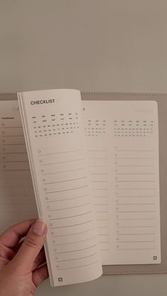 a hand is holding an open planner in front of a wall with calendars on it