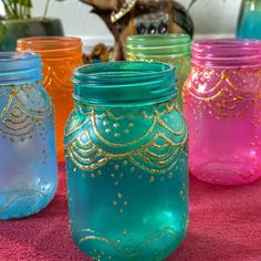 four colorful mason jars sitting on top of a pink tablecloth with gold trimmings