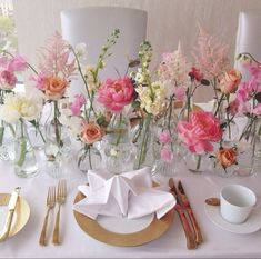 the table is set with pink and white flowers in vases, silverware, and napkins