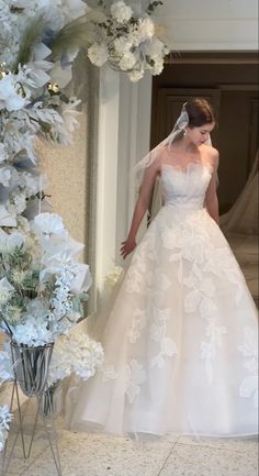 a woman in a white wedding dress standing next to a flower arch with flowers on it