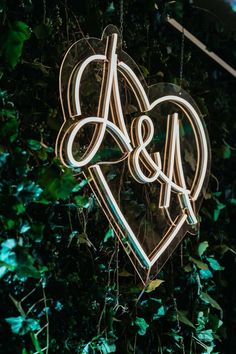 a heart shaped neon sign hanging from the side of a wall covered in greenery