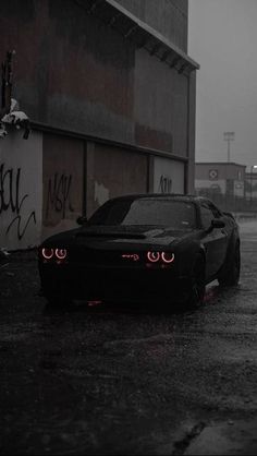 a black sports car parked in front of a building on a rainy day with red eyes