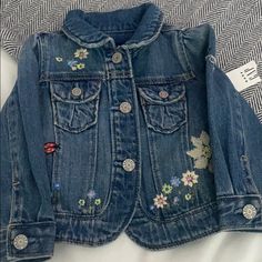 a denim jacket with flowers on the front and back, sitting on top of a bed