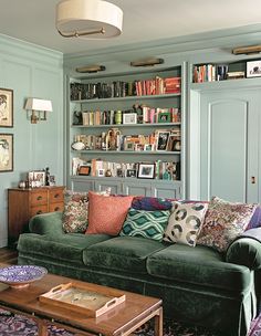 a living room filled with green couches and bookshelves next to a coffee table