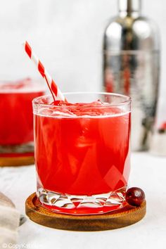 a red drink in a glass with a straw sticking out of the top and another beverage behind it