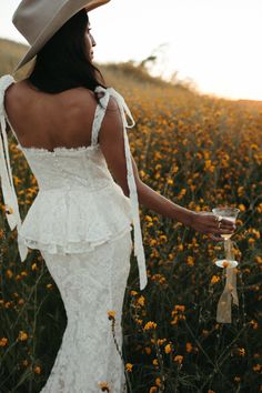 a woman in a white dress and cowboy hat walking through a field with yellow flowers