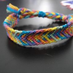 a colorful braided bracelet sitting on top of a black table next to a pair of scissors