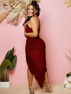 a woman standing in front of a pink wall wearing a red dress with fringes