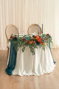 the table is set with two chairs and an arrangement of flowers, candles, and greenery