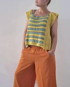 a woman standing in front of a white wall wearing orange pants and a yellow top