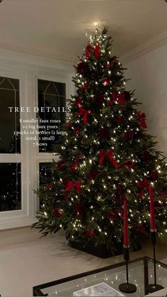 a decorated christmas tree in front of a window with red bows and lights on it