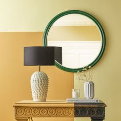 a table with a lamp, mirror and vase on it in front of a yellow wall