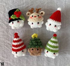 six crocheted christmas ornaments are arranged on a white sheet, including santa's hats and snowmen