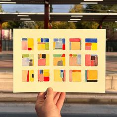 a person holding up a piece of paper with different colored squares on it in front of a gas station