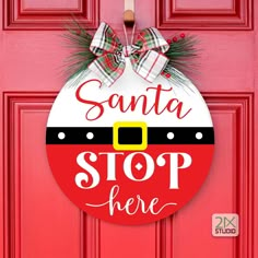 a santa stop here door hanger on a red door with pine cones and plaid bow