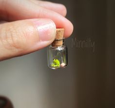 someone is holding a tiny glass bottle with a green frog in it