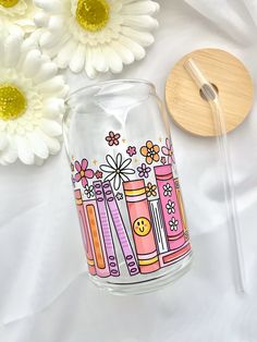 a glass vase with some flowers and a wooden spoon on the table next to it